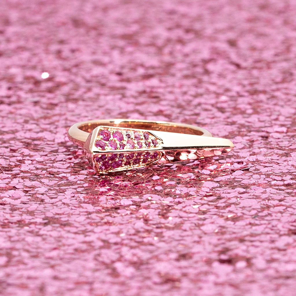 A modern piece of jewelry in rose gold with a natural pink sapphire pavé is photographed on a pink sequins background. It’s a ring in 14k gold designed and crafted in Montreal, Canada, by independent jewellery brand Bena Jewelry. Is is available at Ruby Mardi, a store that specializes in one-of-a-kind jewels.