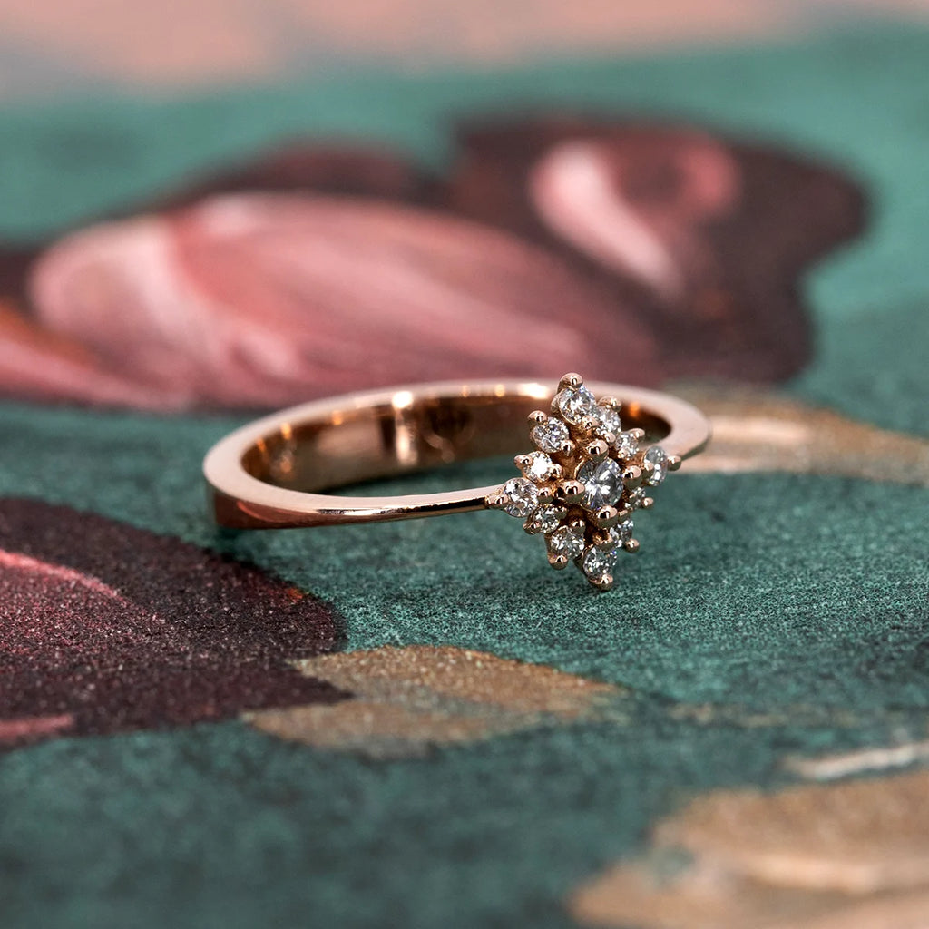 The Solstice ring, a delicate 14k rose gold creation featuring a radiant cluster of diamonds. Inspired by celestial light, this dainty yet dazzling piece captures warmth and brilliance. Photographed on an artistic backdrop, highlighting its refined craftsmanship. Available at Ruby Mardi, an independent jewelry boutique in Montreal offering custom designs.