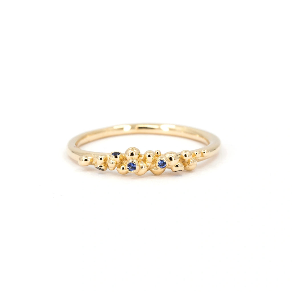 Dainty organic gold ring with scattered blue sapphires, handmade by Meg Lizabet. Minimalist sculptural fine jewelry photographed on white background, available at Ruby Mardi in Montreal.