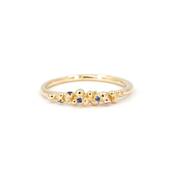 Dainty organic gold ring with scattered blue sapphires, handmade by Meg Lizabet. Minimalist sculptural fine jewelry photographed on white background, available at Ruby Mardi in Montreal.