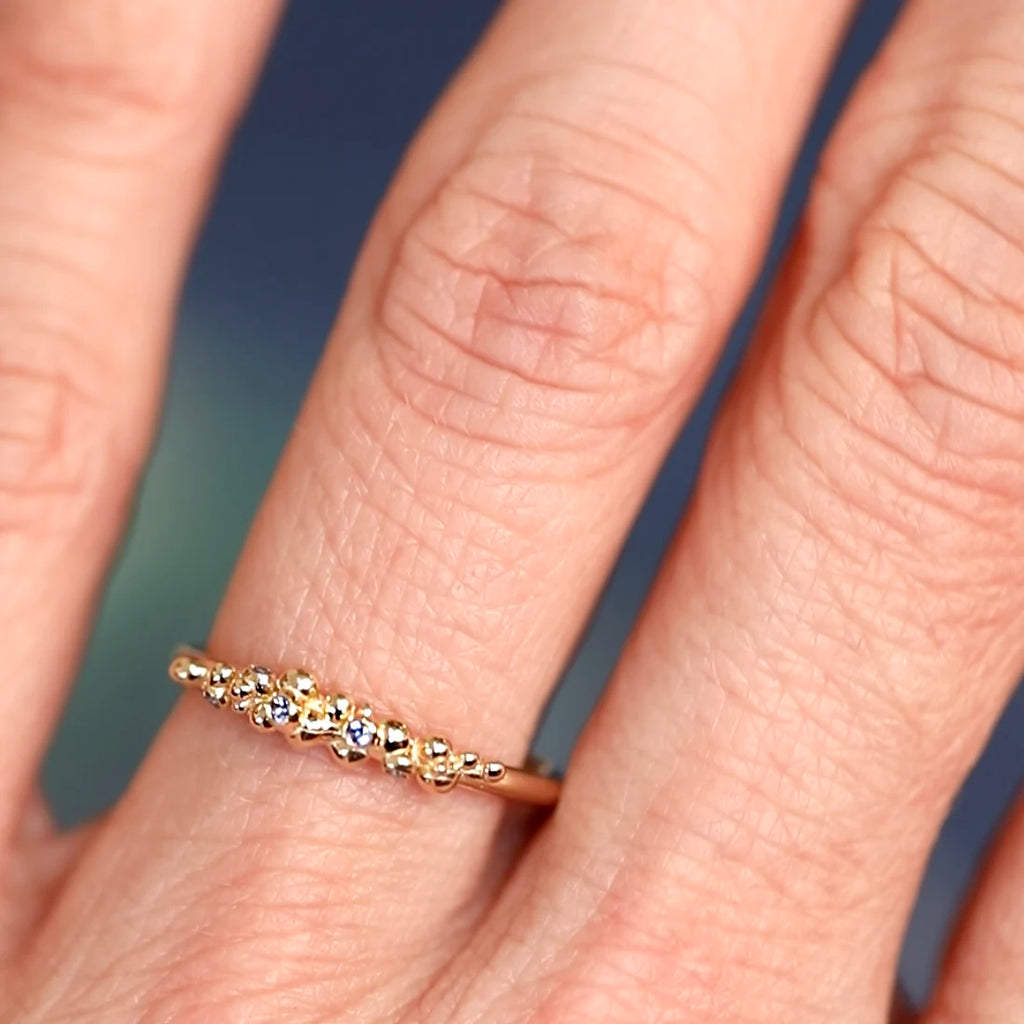 Close-up of a dainty organic gold ring with blue sapphires worn on a finger, handcrafted by Meg Lizabet. Unique fine jewelry available at Ruby Mardi, Montreal.