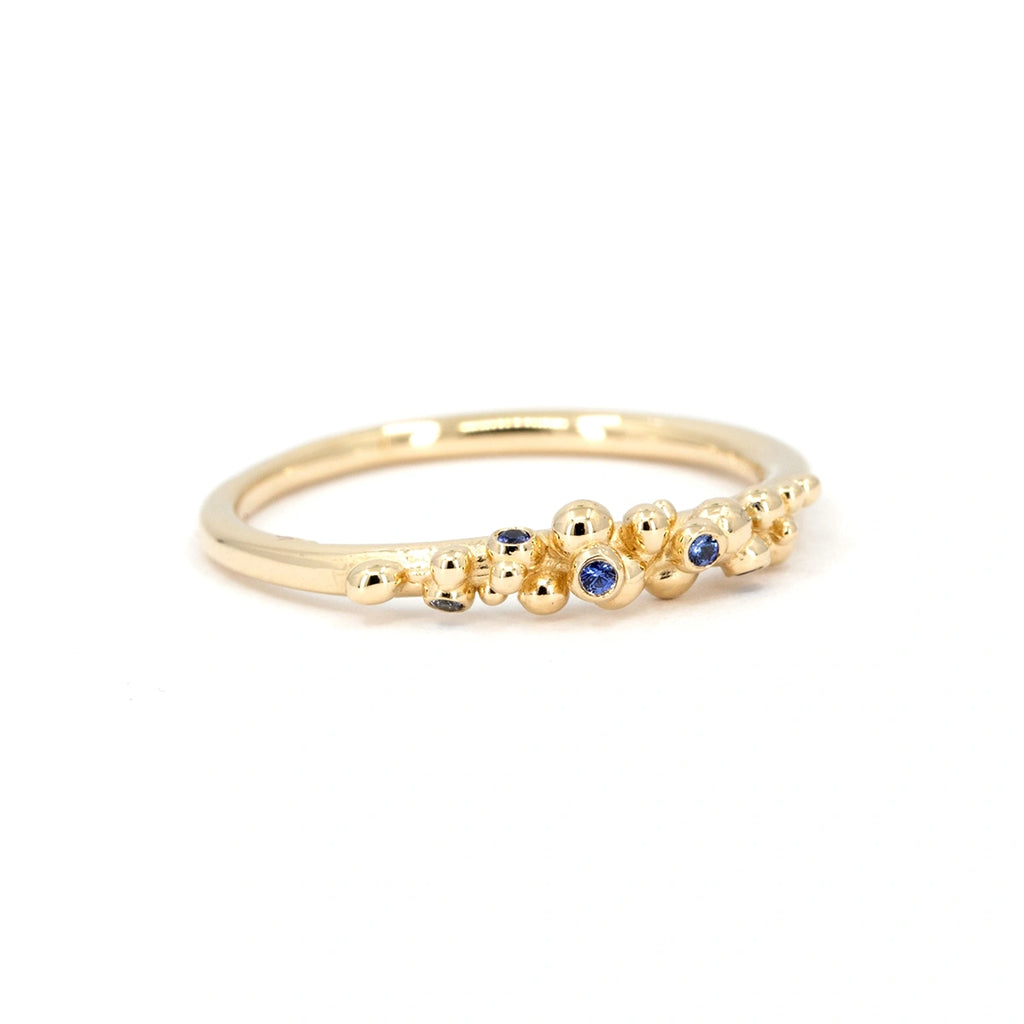 Delicate organic gold ring with blue sapphires and sculptural granule details, handcrafted by Meg Lizabet. Fine contemporary jewelry photographed on white background, available at Ruby Mardi, Montreal.