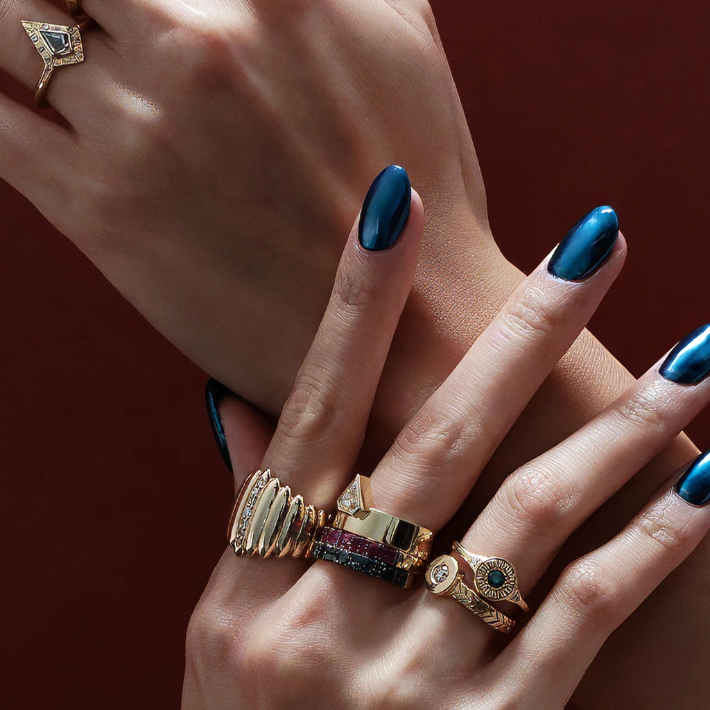 Beautiful studio picture showing two ladie's hand with metallic blue nails wearing multiple Canadian designer rings. The hands wear 7 stunning unique rings from independent jewellers from Montreal, Toronto and Vancouver. All available at Ruby Mardi, an indie jewelry store in Canada.