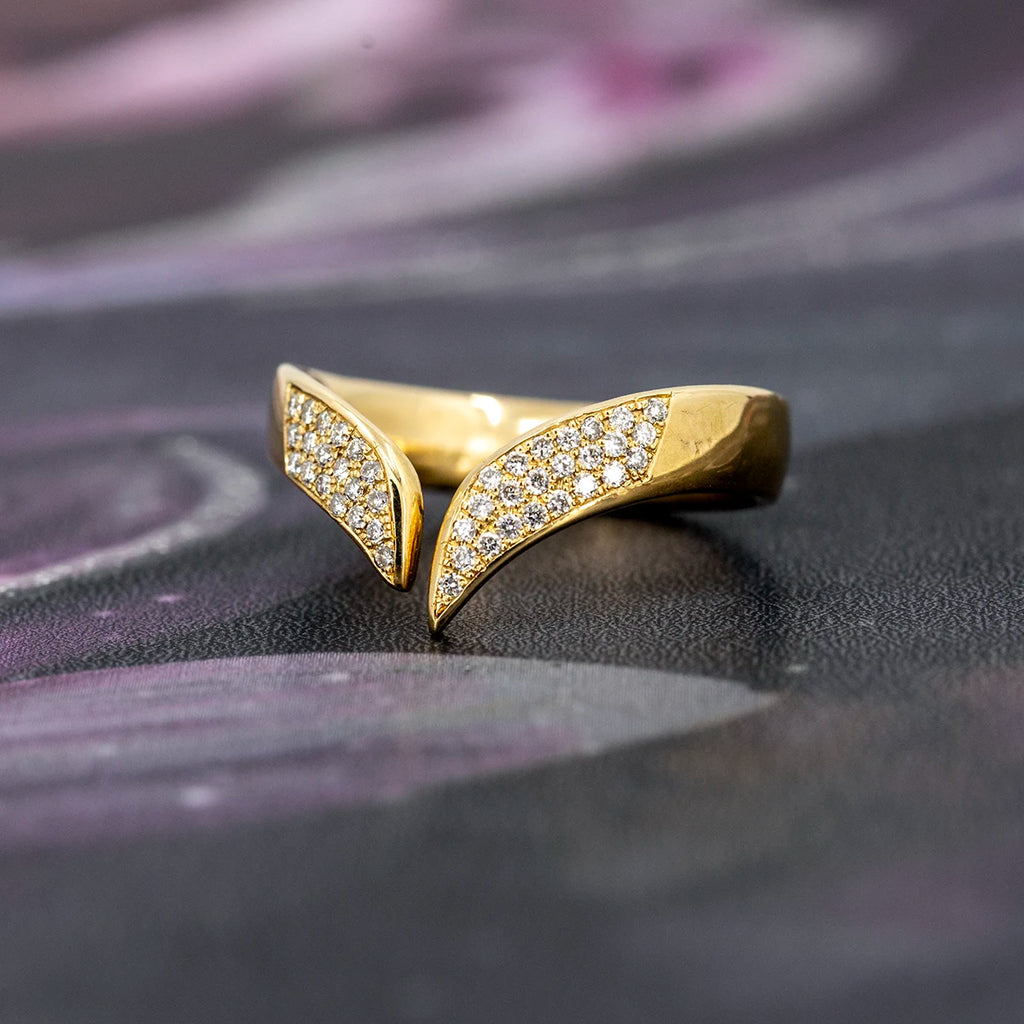 V-shaped diamond band in solid 10k yellow gold by Canadian jeweller Nadia Werchola, shown on a dark, softly textured surface. The front of the ring is fully pavé-set with lab-created diamonds, highlighting its bold open design, tapered contours, and bright reflective finish.