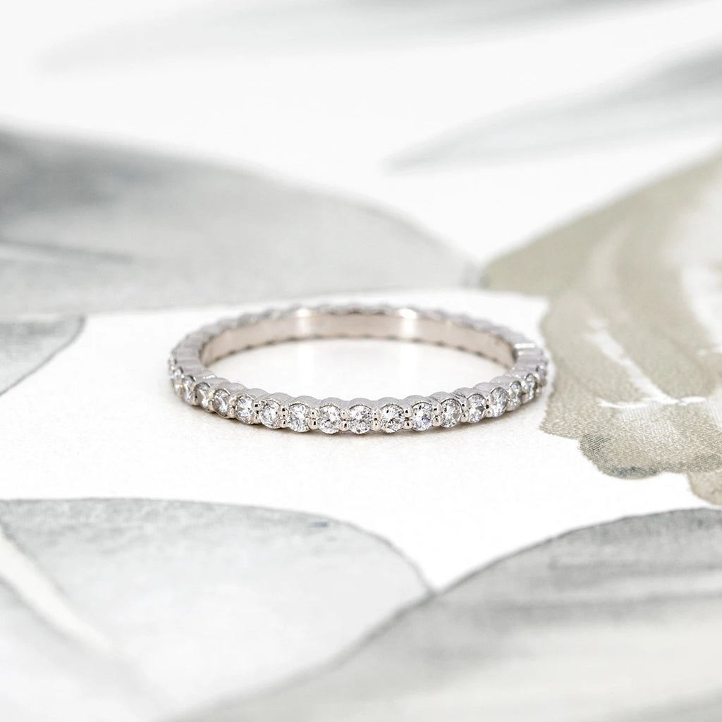 A delicate white gold eternity band featuring 1.5 mm diamonds, handcrafted in Montreal by Ruby Mardi—where custom jewelry services are offered—displayed against a soft floral background.