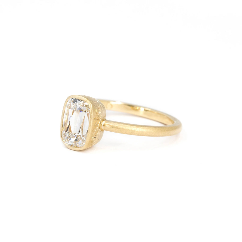 Side view of a diamond solitaire ring with antique cushion cut, set in a matte yellow gold bezel richly engraved with floral motifs. Made in Ottawa by Fluid Jewellery with Fairmined gold. Ethical and one-of-a-kind engagement ring available at Ruby Mardi, Montreal.