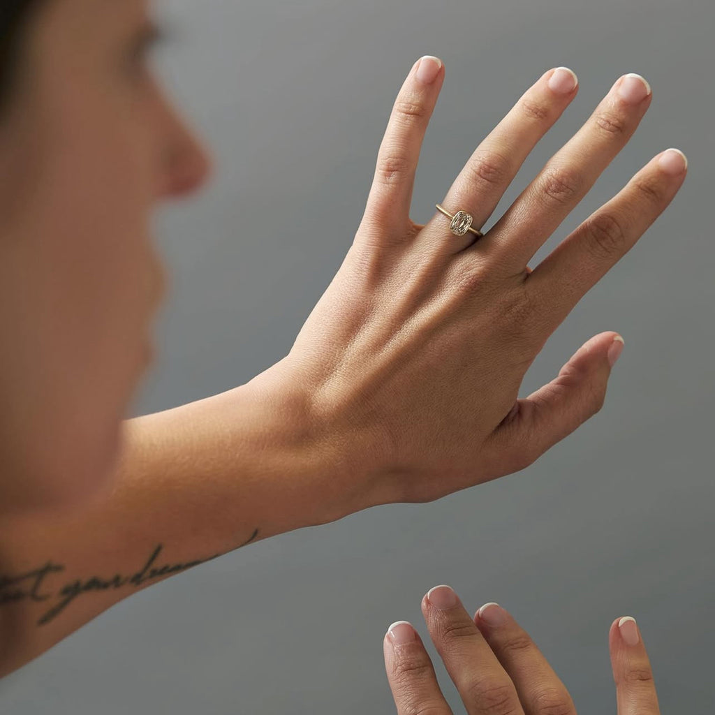 Close-up of a hand wearing a diamond solitaire ring with matte yellow gold band and hand-engraved details. Elegant minimalist jewelry handcrafted in Montreal, available at Ruby Mardi.