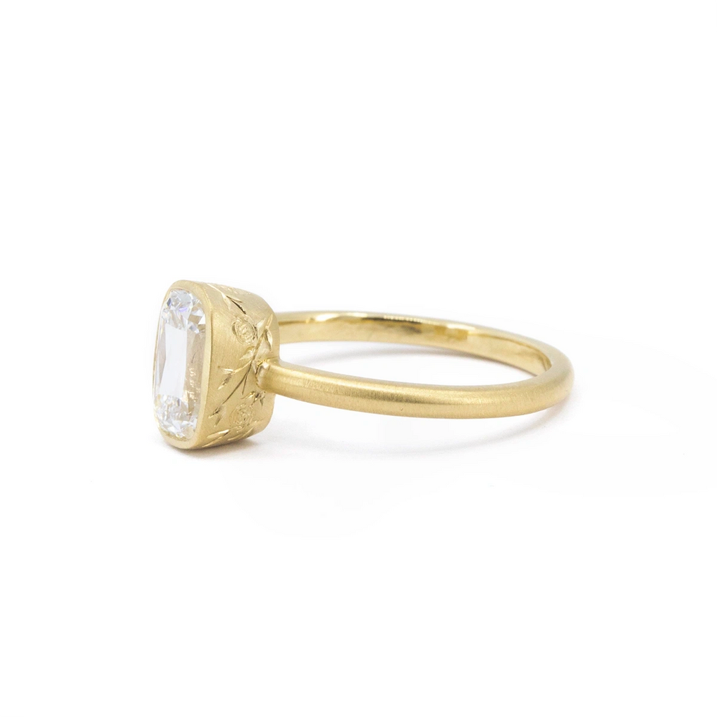 Diamond solitaire ring in Fairmined yellow gold with bold hand-engraved floral details on a wide bezel, showcasing a 1.25 ct antique cushion-cut diamond. Made in Ottawa by Fluid Jewellery, available at Ruby Mardi.