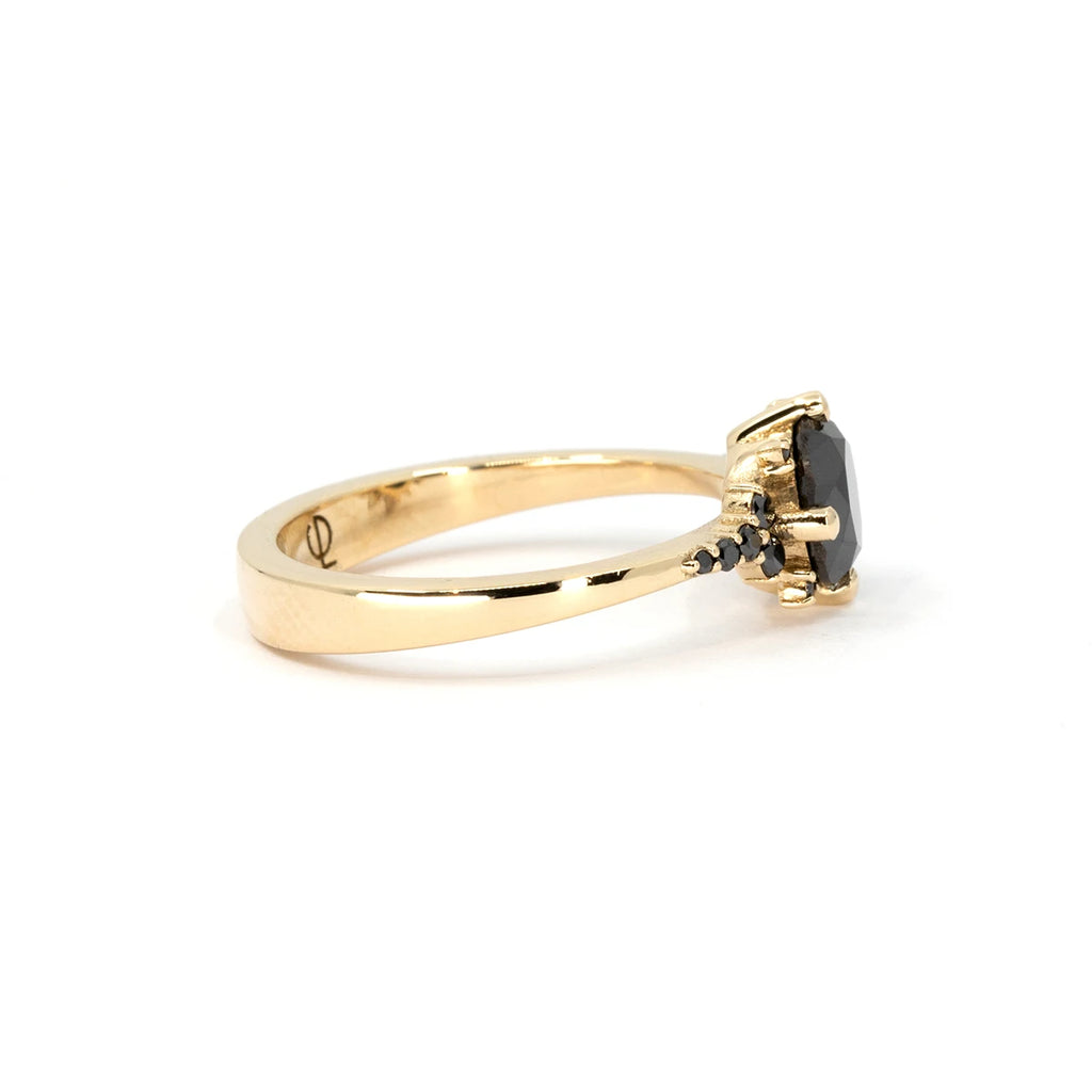 Side view of the Éclipse ring, a 14k yellow gold design featuring a bold round-cut black diamond in a claw setting. Delicate black diamond accents and intricate gold bead details enhance the celestial-inspired aesthetic. Available at Ruby Mardi, an independent jewelry boutique in Montreal offering custom jewelry services.