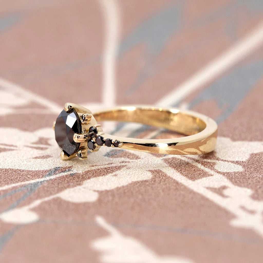 Gold engagement ring featuring a round black diamond in a claw setting, accented with smaller black diamonds along the band. Designed by Oleg Leybman, this unique and edgy piece is available at Ruby Mardi, a Montreal-based jewelry store specializing in designer jewelry.