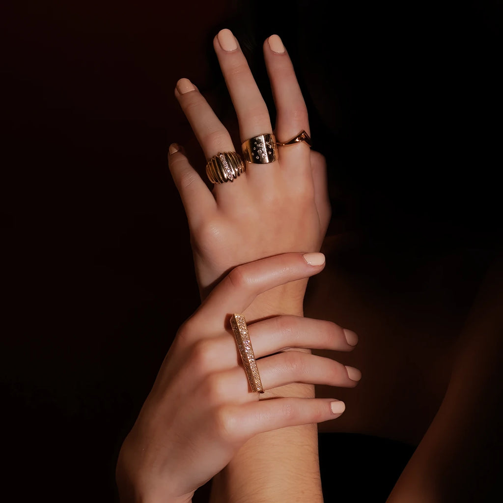 Studio high end jewelry fashion shoot. Dark background almost black. All that lights up are two women's hands wearing luxurious yellow gold and diamond jewelry, all created by independent Canadian brand Bena Jewelry.