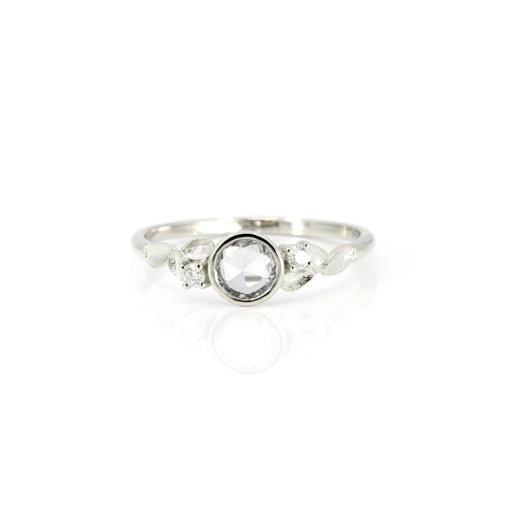 This splendid white gold ring with a rose cut white sapphire and a delicate petal-shaped ring made by independent jewelry designer Émigé. This delicate and alternative engagement ring is available for sale at the Ruby Mardi jewelry store located in Montreal.