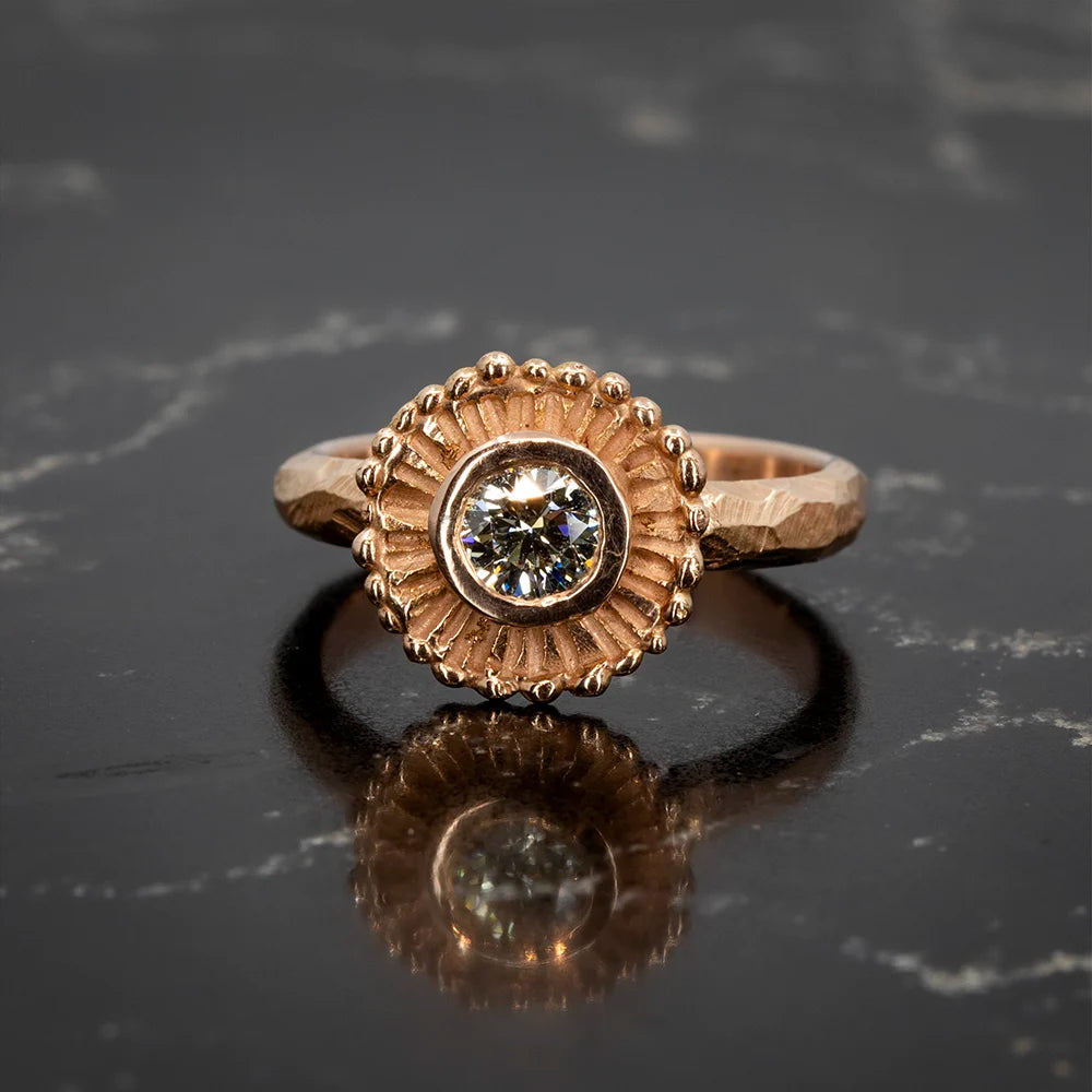 Gold ring with a round brilliant diamond set in a textured bezel, surrounded by a sunburst design. Crafted by Emma Glover, available at Ruby Mardi in Montreal.