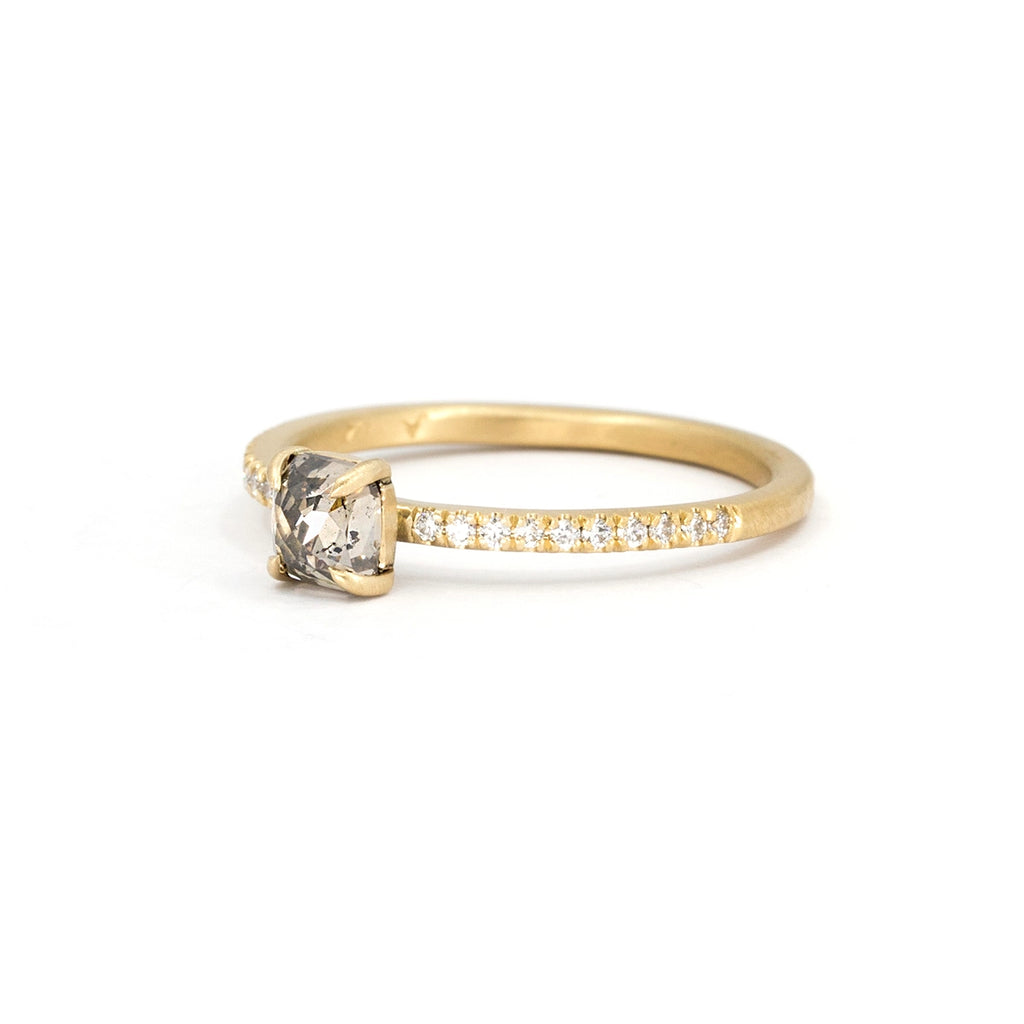 Viewed from the side against a white background, a solitaire engagement ring with a small central salt-and-pepper cushion diamond, claw prongs, natural round diamonds set on the band, and a satin finish unique to the independent Fluid Jewellery brand. The photo was taken by Ruby Mardi, a fine jewelry store that sells the work of Canada's finest jewelry designers. 