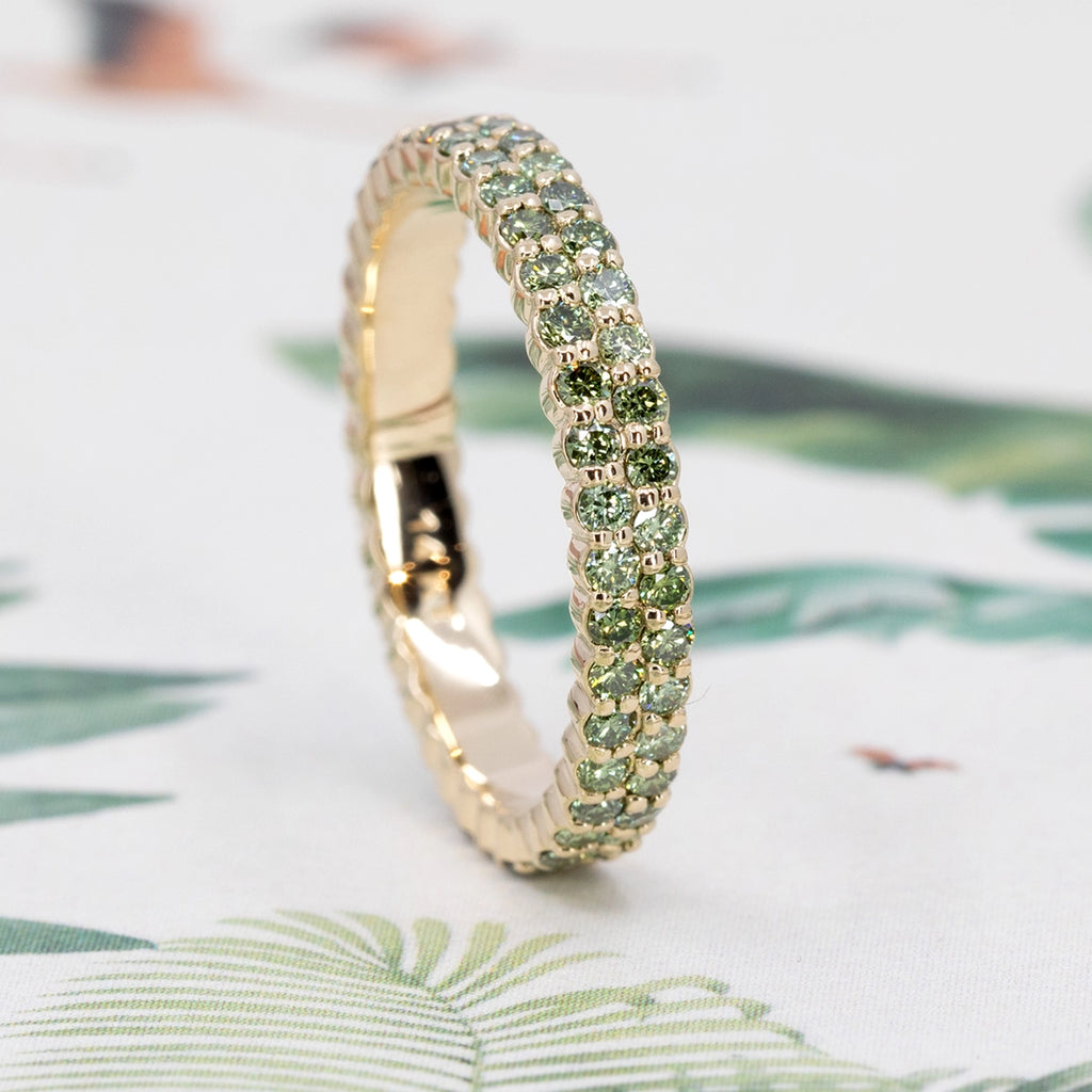 Side view of the Ruby Mardi green diamond eternity band, featuring two rows of round green diamonds set in yellow gold. Contemporary Canadian fine jewelry photographed on a botanical background.