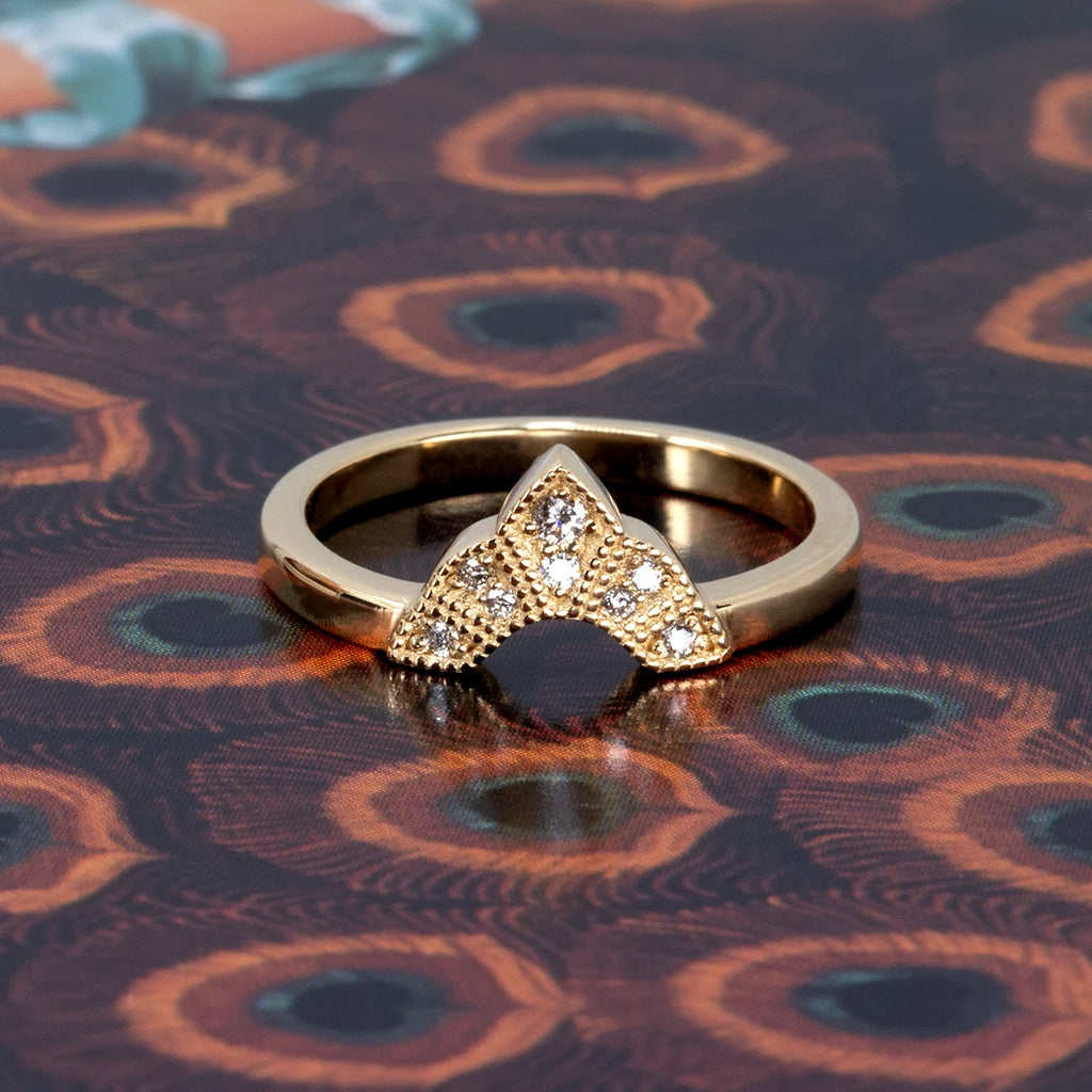 V-shaped yellow gold ring with natural diamonds and Art Deco milgrain details, shown stacked on a peacock feather print background. Designed by Deborah Lavery for Ruby Mardi.