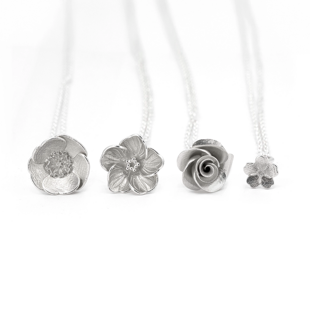 Collection of white gold wildflower pendants by Fleurs Sauvages Qc displayed side by side, including buttercup, wood sorrel, rose and myosotis designs. Handmade botanical jewelry available at Ruby Mardi in Montreal.