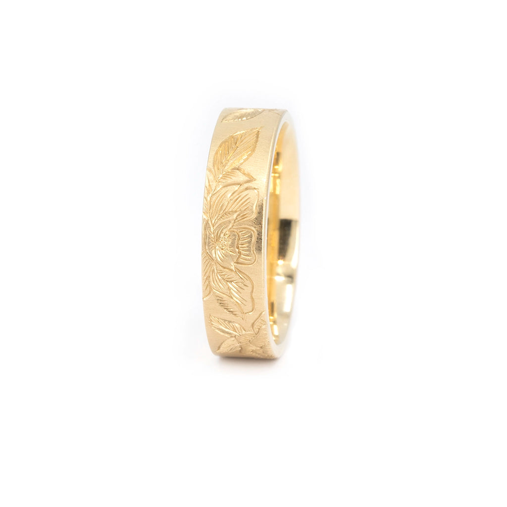 14k yellow gold band with hand-engraved flowers and leaves, crafted by Rebel & Rogue. The matte background enhances the engraving depth. Photographed for Ruby Mardi in Montreal, Canada, highlighting artisan wedding jewelry.