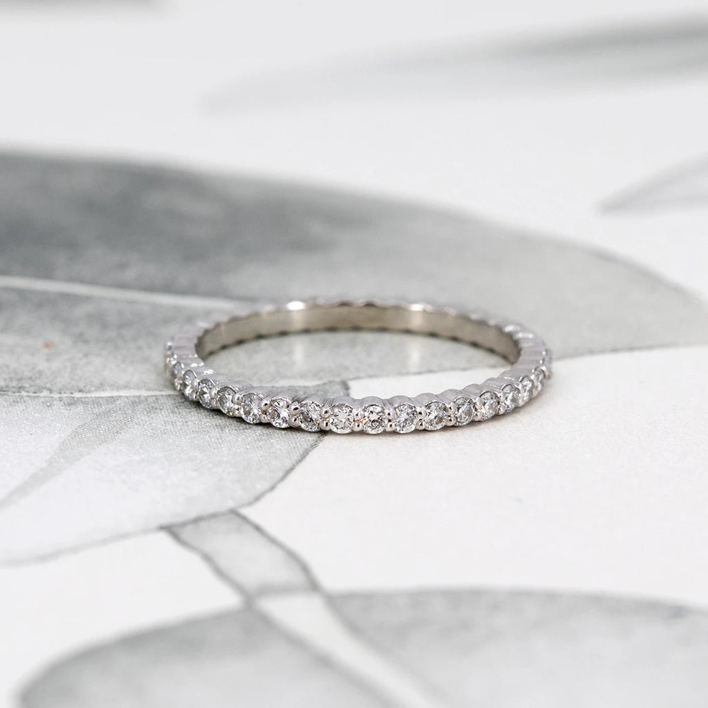 A close-up of a delicate white gold diamond eternity band featuring 1.5 mm diamonds, handcrafted in Montreal by Ruby Mardi, resting on a soft floral background.