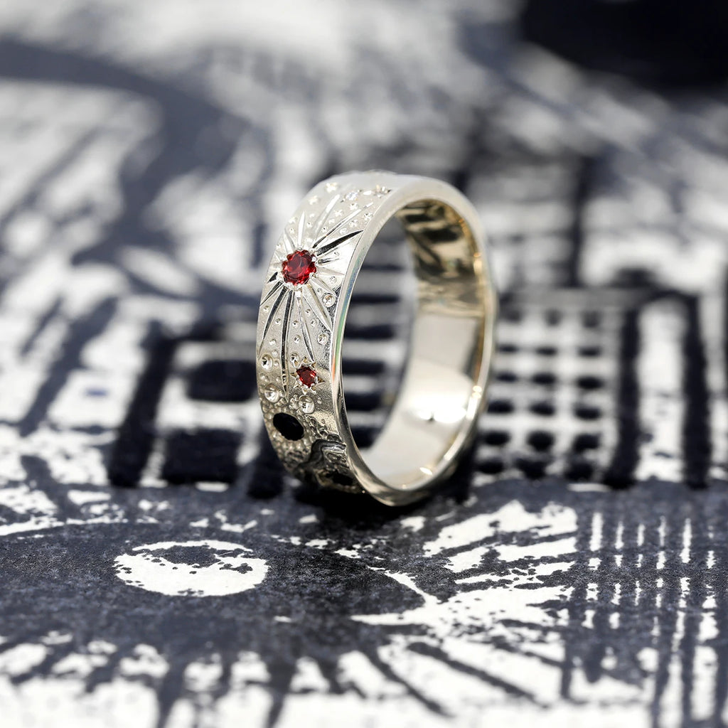 The Galaxy Newton ring is a wedding band made of gold with handmade engravings and decorated with several colored gems, including red and black. This exclusive piece of jewelry is custom-made in Canada by independent designer Janine de Dorigny and available for sale at the Ruby Mardi jewelry store located in Montreal.