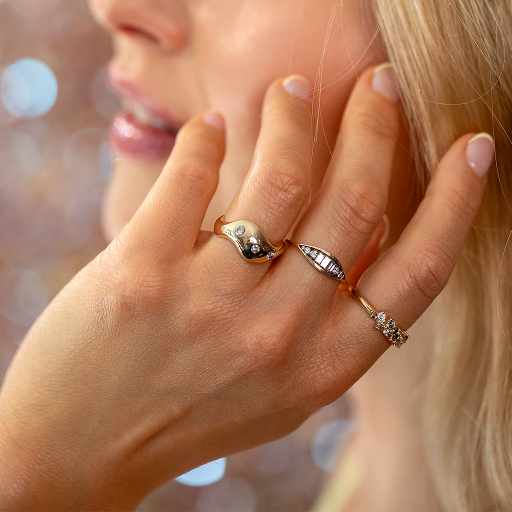 Close-up of a woman wearing three gold designer rings with diamonds, handcrafted by Canadian jewelers and available at Ruby Mardi, a fine jewelry boutique in Montreal.