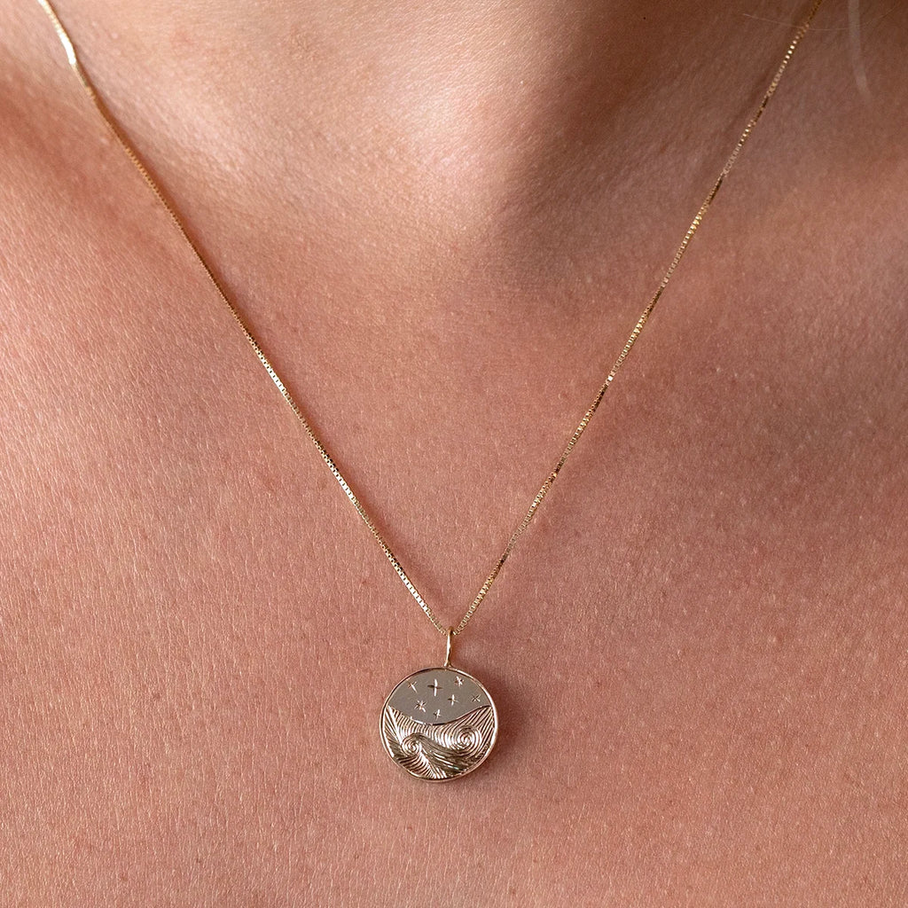 Gold pendant necklace with hand-engraved waves and starry sky motif, worn close to the neck. Fine jewelry by Ruby Mardi, Canadian designer.