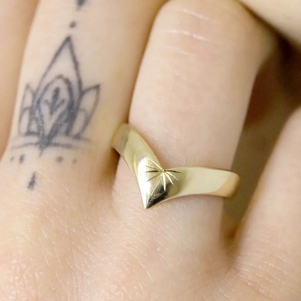 Woman's hand wearing a gold spade-shaped ring. This fine piece of jewelry is quite large on the finger and it has a handmade engraving by independent jewelry designer Nadia Wercola in Canada in collaboration with Montreal's best jewelry store, Ruby Mardi jeweler.