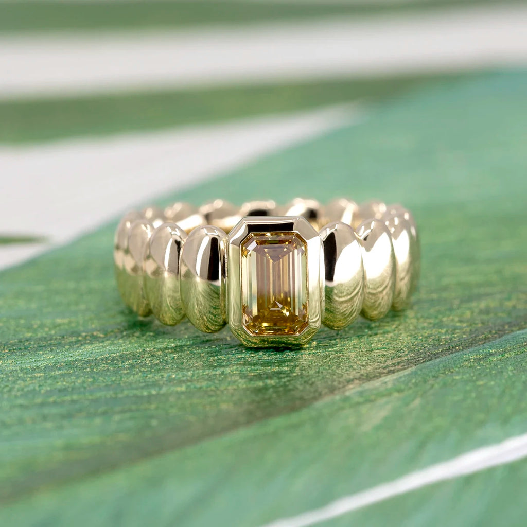 Golden cocktail ring with a radiant yellow diamond center, designed by Bena Jewelry and photographed on a green patterned background.