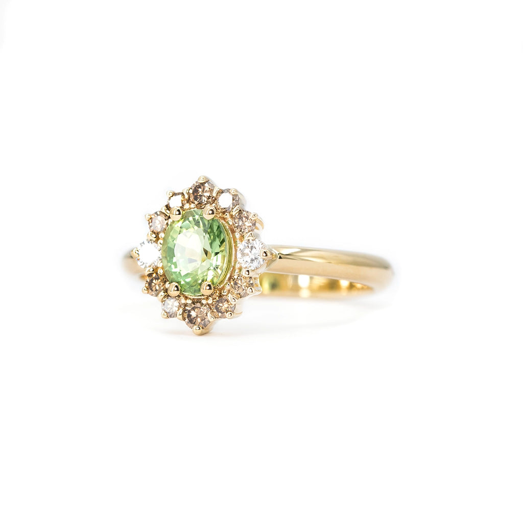 Yellow gold engagement ring with an oval green sapphire, surrounded by a halo of champagne and white diamonds.