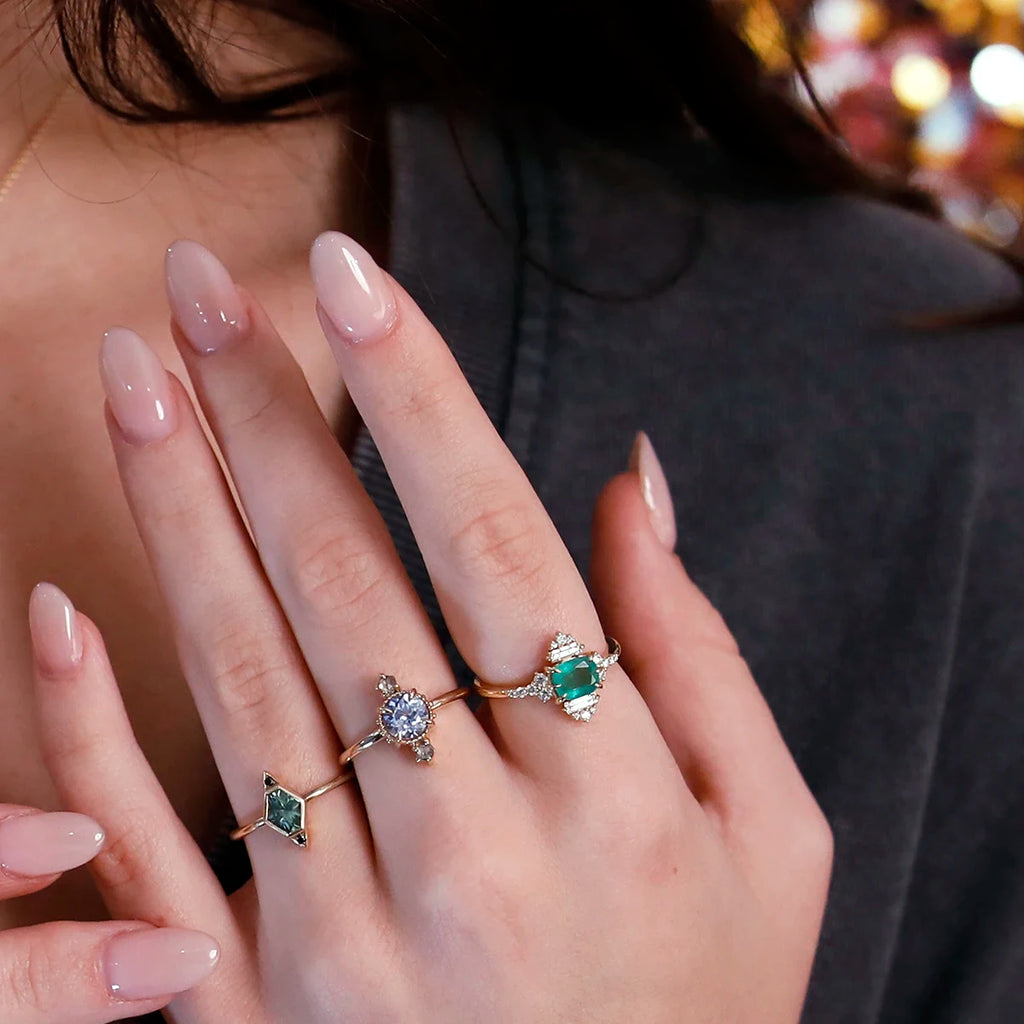 Hand-shot of a model wearing three unique gold rings featuring a green Montana sapphire, an emerald, and a lavender sapphire. Designed by independent Canadian jewelers, available at Ruby Mardi in Montreal.