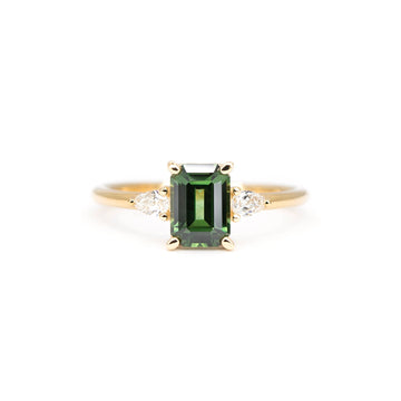 Front view of an engagement ring featuring an emerald-cut green sapphire flanked by two pear-shaped diamonds, set in 14k yellow gold. Ruby Mardi, Montreal.