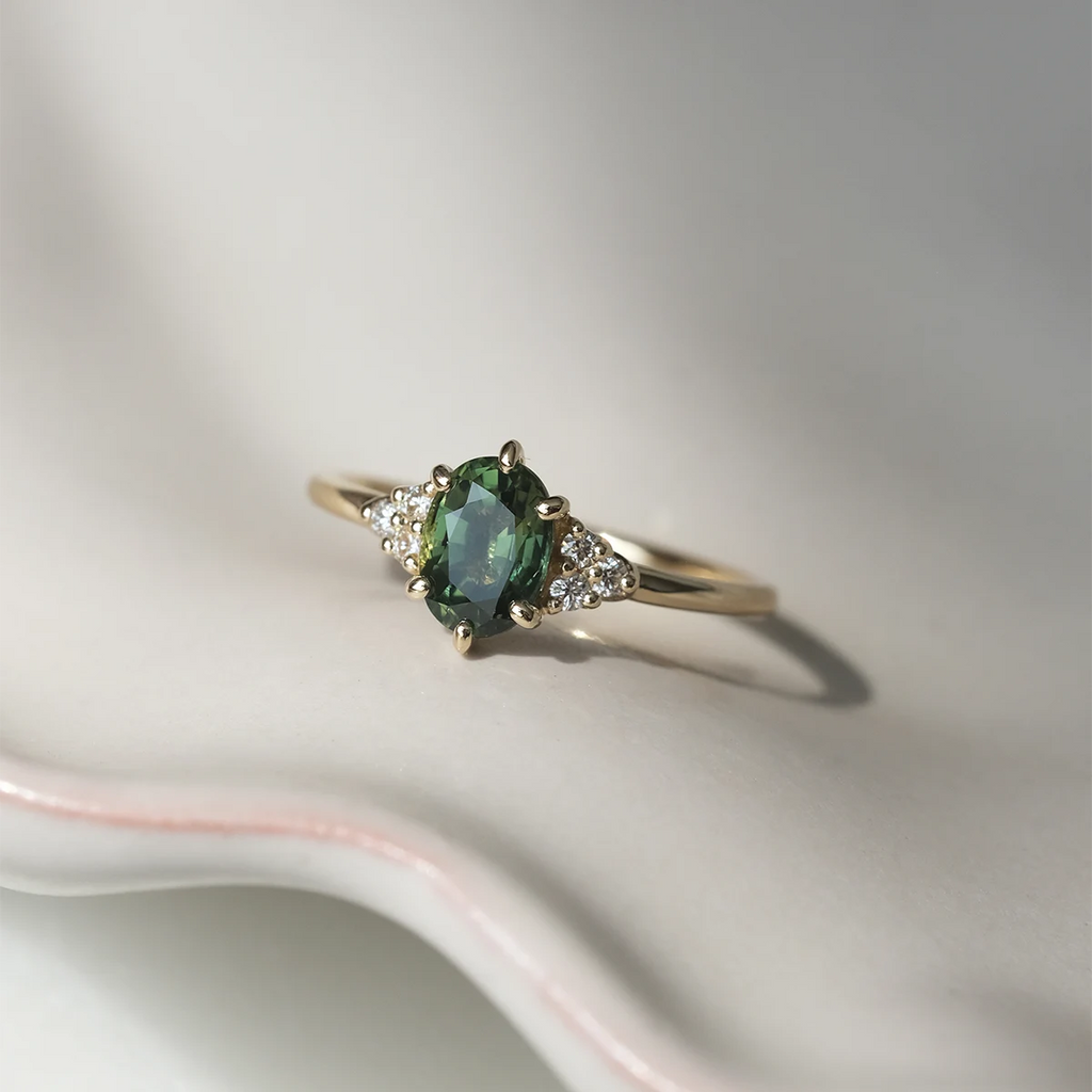 Green sapphire engagement ring with diamond clusters on ceramic tray. Handmade in Montreal by Maksym Jewelry, available at Ruby Mardi.