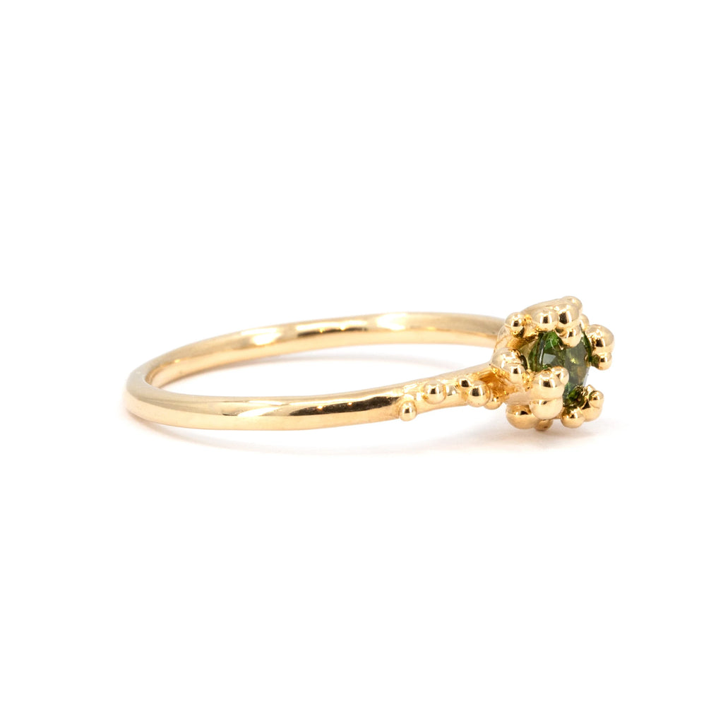 A side view of a green sapphire solitaire ring featuring intricate organic gold bead accents. This delicate and unique piece, crafted by Meg Lizabet, is available at Ruby Mardi in Montreal, showcasing fine artisanal craftsmanship.