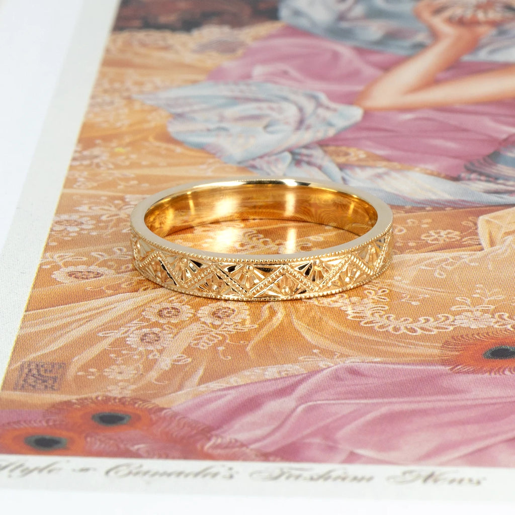 14k yellow gold Art Deco wedding band with hand-engraved geometric patterns and milgrain edges, photographed on a vintage-style illustration. Designed by Deborah Lavery, available at Ruby Mardi in Montreal.