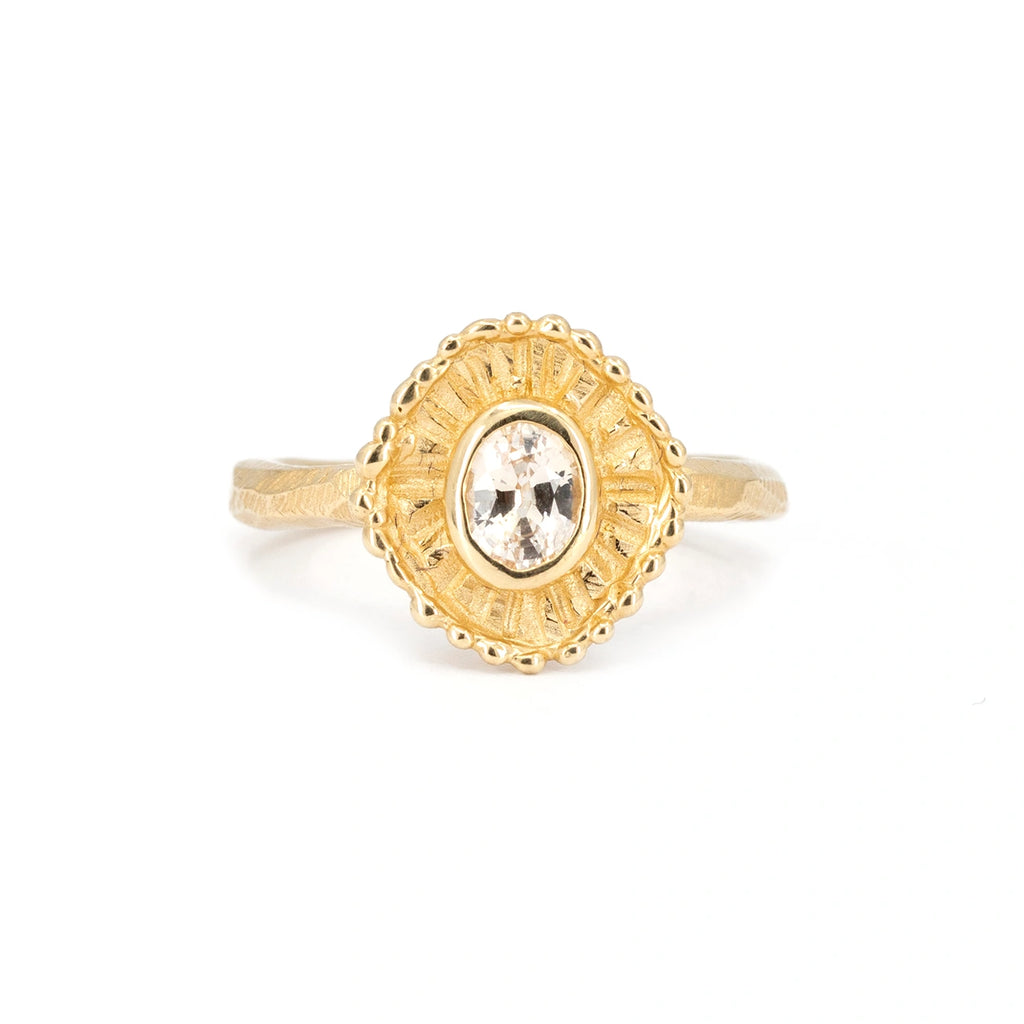Organic gold ring seen from face on a white background. This handmade engagement ring is from indie designer Emma Glover. It shows a central light peach sapphire bezel set  surrounded by gold in the shape of a shell.