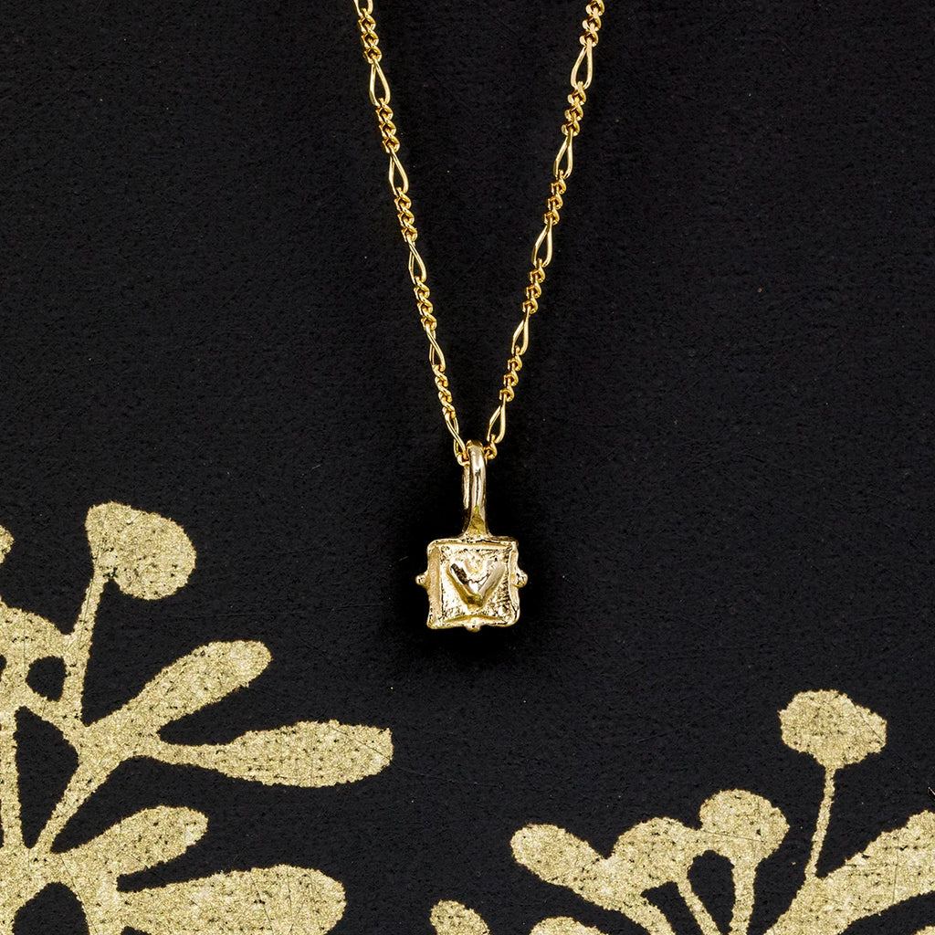 A 10k yellow gold pendant with a raised heart design, photographed from the front against a sleek black and gold background. Designed by Emma Glover, available at Ruby Mardi, Montreal. Simple elegance with a refined touch.