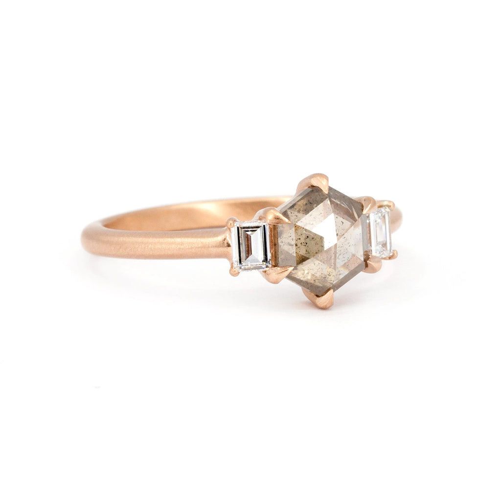 Side view of a classic rose gold engagement ring with a hexagonal champagne diamond and two baguette-cut white diamonds, set with eagle claws, photographed against a white background. Made with Fairmined-certified gold by Ottawa-based independent brand Fluid Jewellery. A fine jewelry piece available at Ruby Mardi, a jewelry store specializing in unique designer jewelry, as Gem Breakfast does.