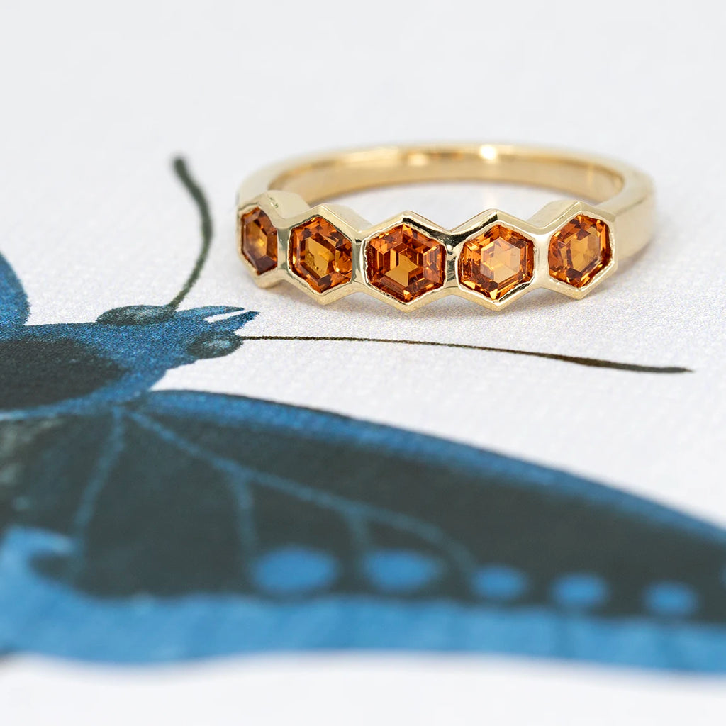The Honeycomb ring in yellow gold with spessartite garnets in a bezel setting is made by the jeweler and artisans In the Light of Day. This fine, edgy piece of jewelry is available for sale at the Ruby Mardi jewelry store in Montreal, a specialist in contemporary jewelry in Canada.