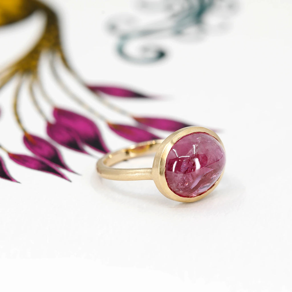 Handmade gold ring featuring a big central ruby cabochon. The one-of-a-kind ring is seen photographed on a colorful background. 