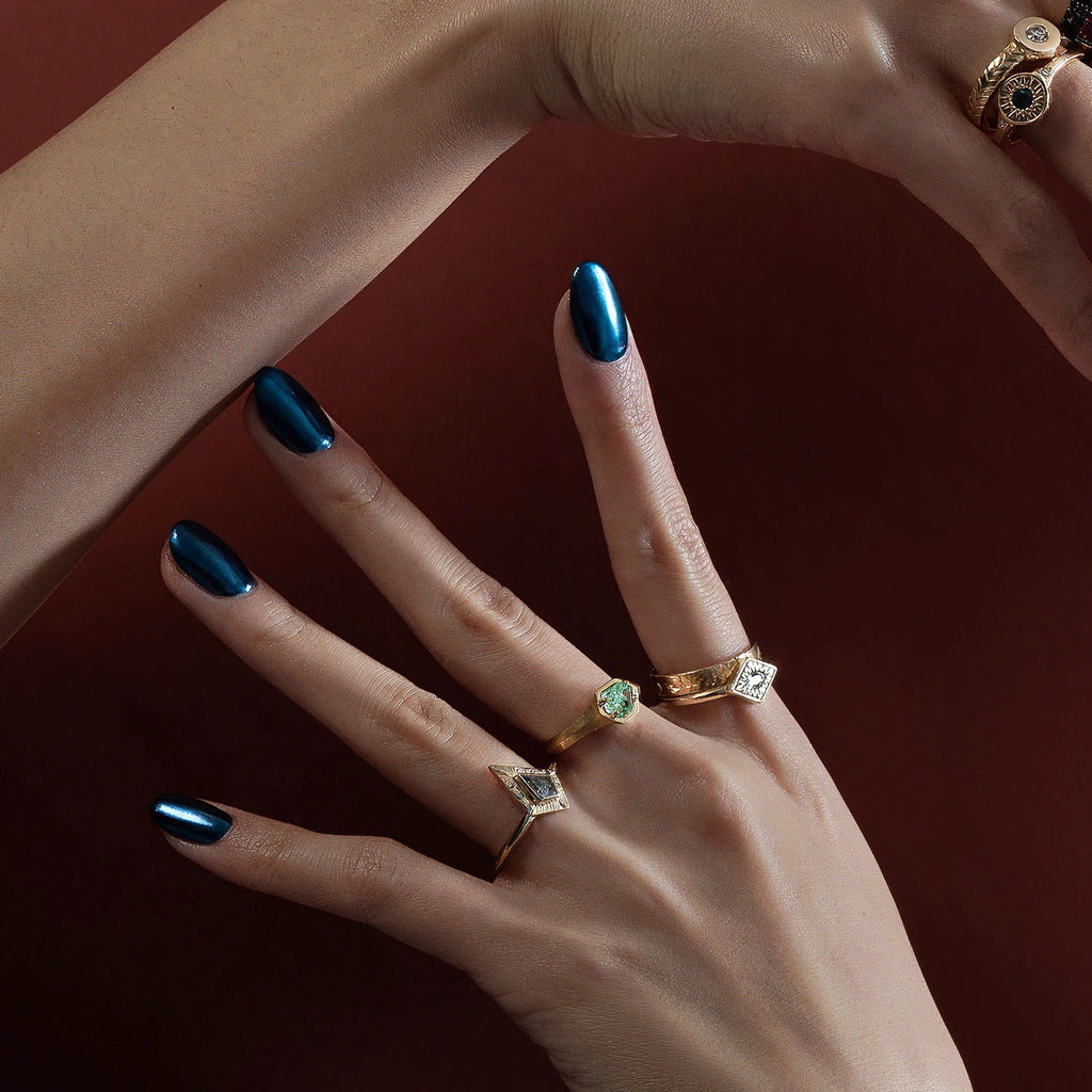 An artistic photograph of two hands elegantly placed to showcase 5 independent designer rings. The hands wear electric blue nail polish. The rings shown are all handcrafted and feature ethical gemstones. Ruby Mardi sells its unique jewelry exclusively in Canada.