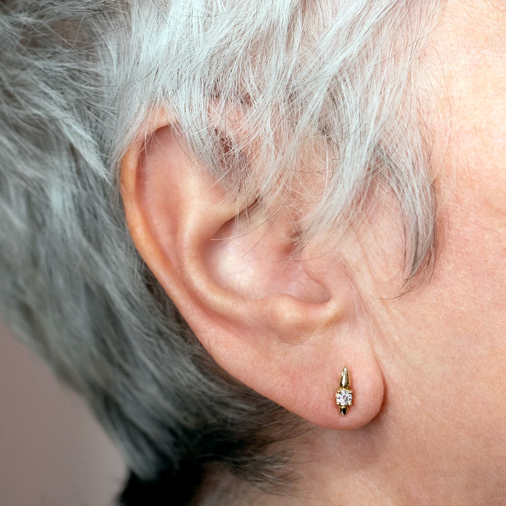 14k yellow gold earrings with sparkling diamonds, worn by an elderly woman with white and grey hair. The close-up shot highlights the elegance and brilliance of the earrings, adding a refined touch of light to the ear.