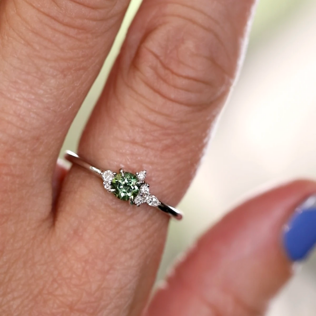 Little Folie ring in 18k white gold by Justine Quintal, featuring a dark teal sapphire and diamond accents, shown worn on a hand.