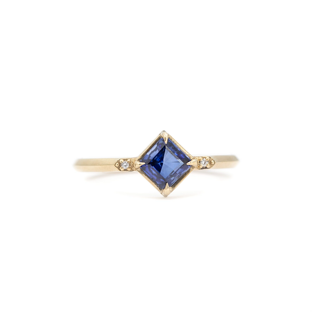 Square blue sapphire engagement ring set on yellow gold band with small diamond accents, minimalist fine jewelry by Liane Vaz for Ruby Mardi.