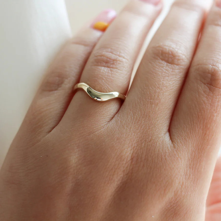 Curved 14k gold wave wedding band worn on a hand, designed by Canadian jeweller Yuliya Chorna. Available at Ruby Mardi, a fine jewelry boutique in Montreal.