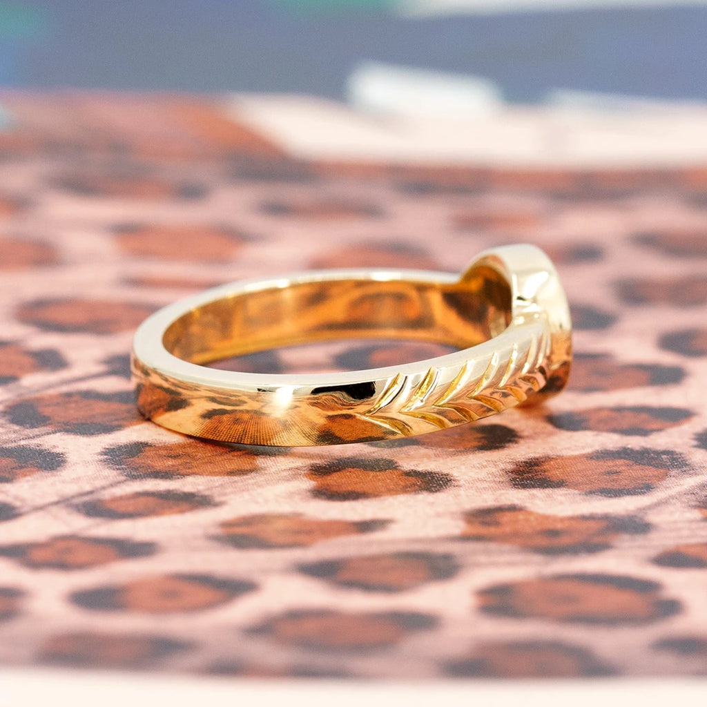Back view of a bold gold ring photographed on a pink leopard design. The ring has hand engraved details. It was designed by independent jeweller Savannah Jones. 