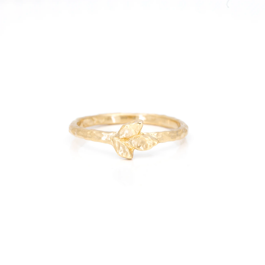 A simple yellow gold hammered wedding band showing a leaf detail is photographed on a white background. The ring has an organic feel and shows 3 leaves on its center. It was handmade by Canadian independent jewellery brand Anouk Jewelry, and it is available online and in Montreal at Ruby Mardi.