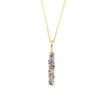 Gold necklace featuring a vertical bar pendant set with a graduated row of light blue sapphires in prong settings. Organic designer jewelry by Meg Lizabet, Montreal, Canada.