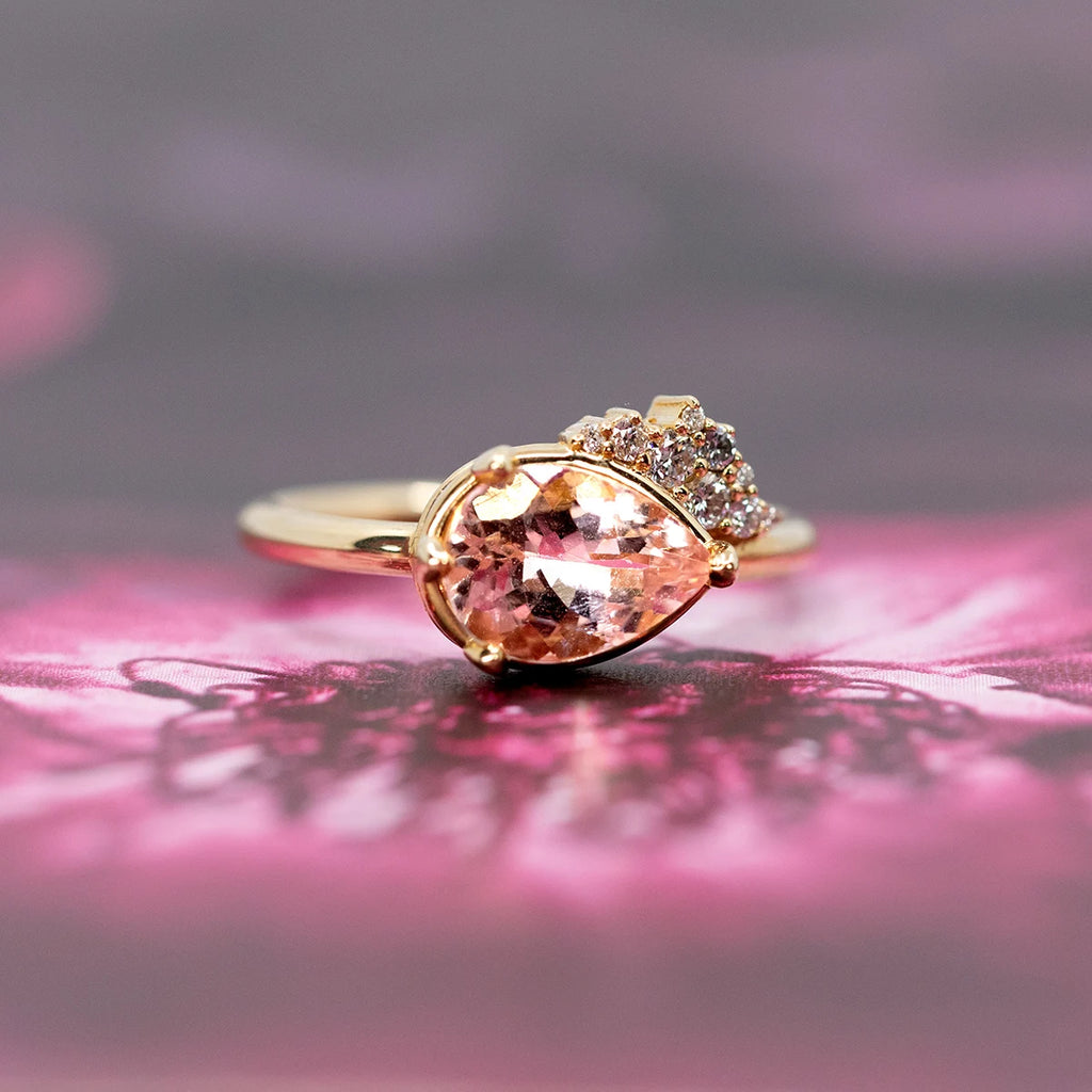 A stunning pear-shaped morganite engagement ring, featuring a blush-pink gemstone at its center. The asymmetrical design is elevated with a radiant cluster of brilliant-cut diamonds that add texture and sparkle. Crafted in 14k yellow gold, this elegant piece is both modern and romantic, showcasing Sheena Purcell’s signature artistry. Handcrafted in Montreal and available exclusively at Ruby Mardi.