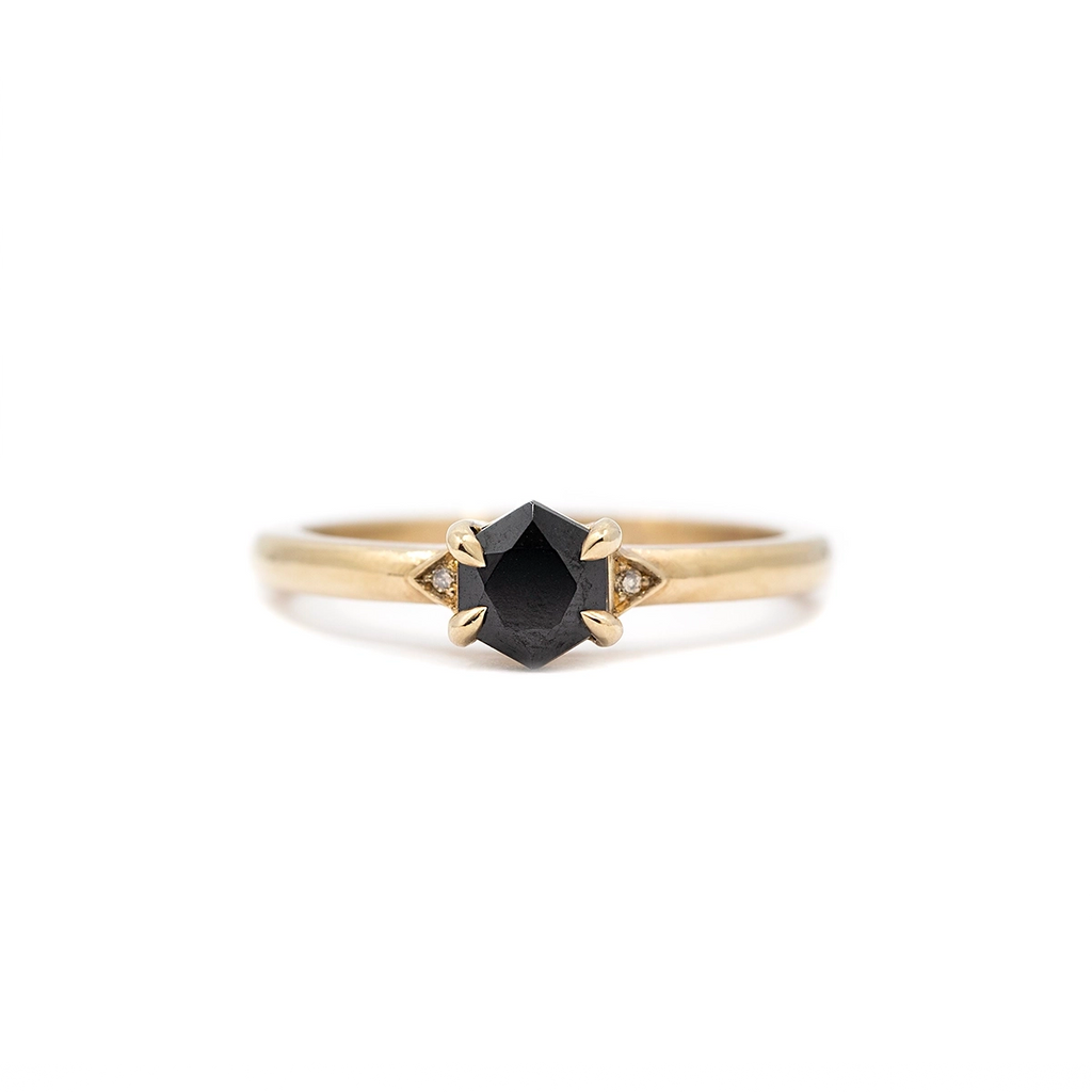 Close-up product image of the Luna Hex ring by Liane Vaz, featuring a hexagon-cut black spinel center stone flanked by two tiny champagne diamonds, set in a polished yellow gold band. The ring is photographed against a plain white background for Ruby Mardi jewelry in Montreal, Canada.