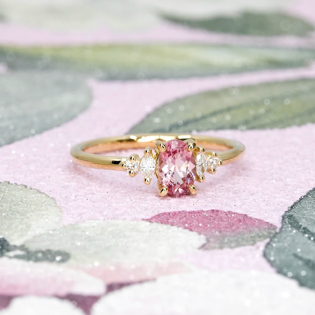 Yellow gold ring with Malaya garnet and diamond accents, photographed on a pastel floral background. Handmade by Maksym for Ruby Mardi in Montreal, Canada.